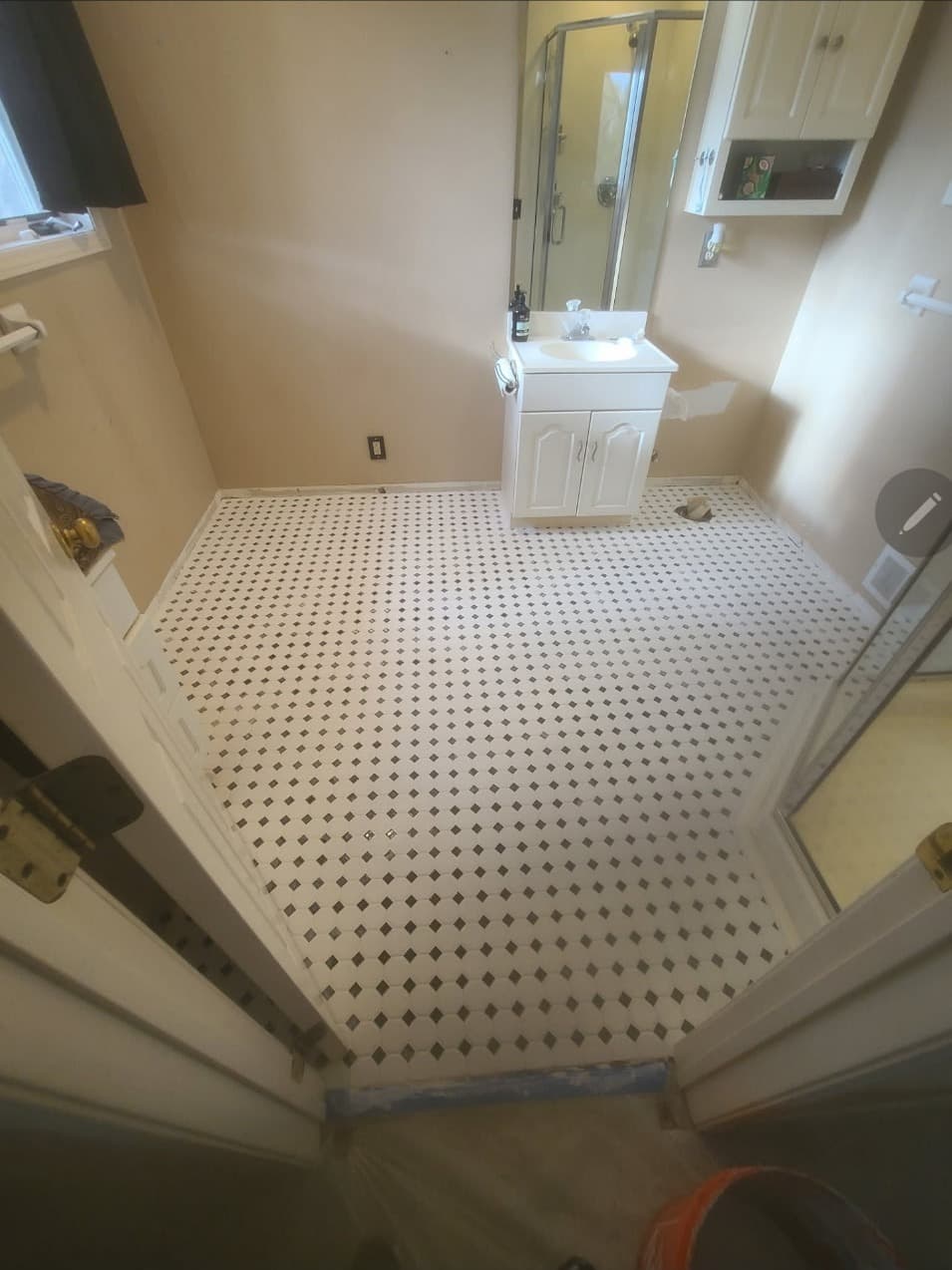 Bathroom with black and white mosaic tile floor, white vanity and glass shower door