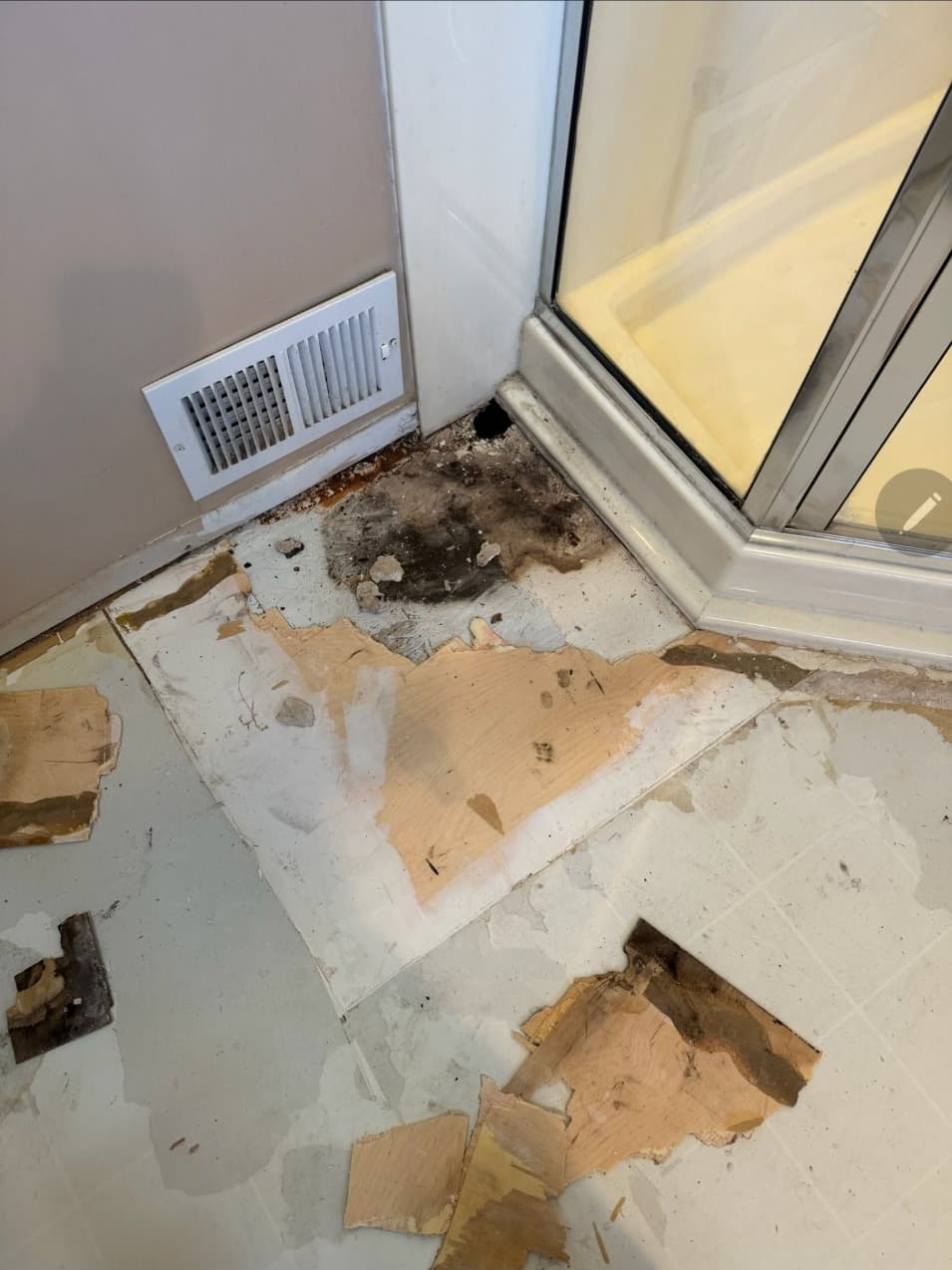 Damaged bathroom subfloor cut out for repair next to a glass shower in Minneapolis, MN
