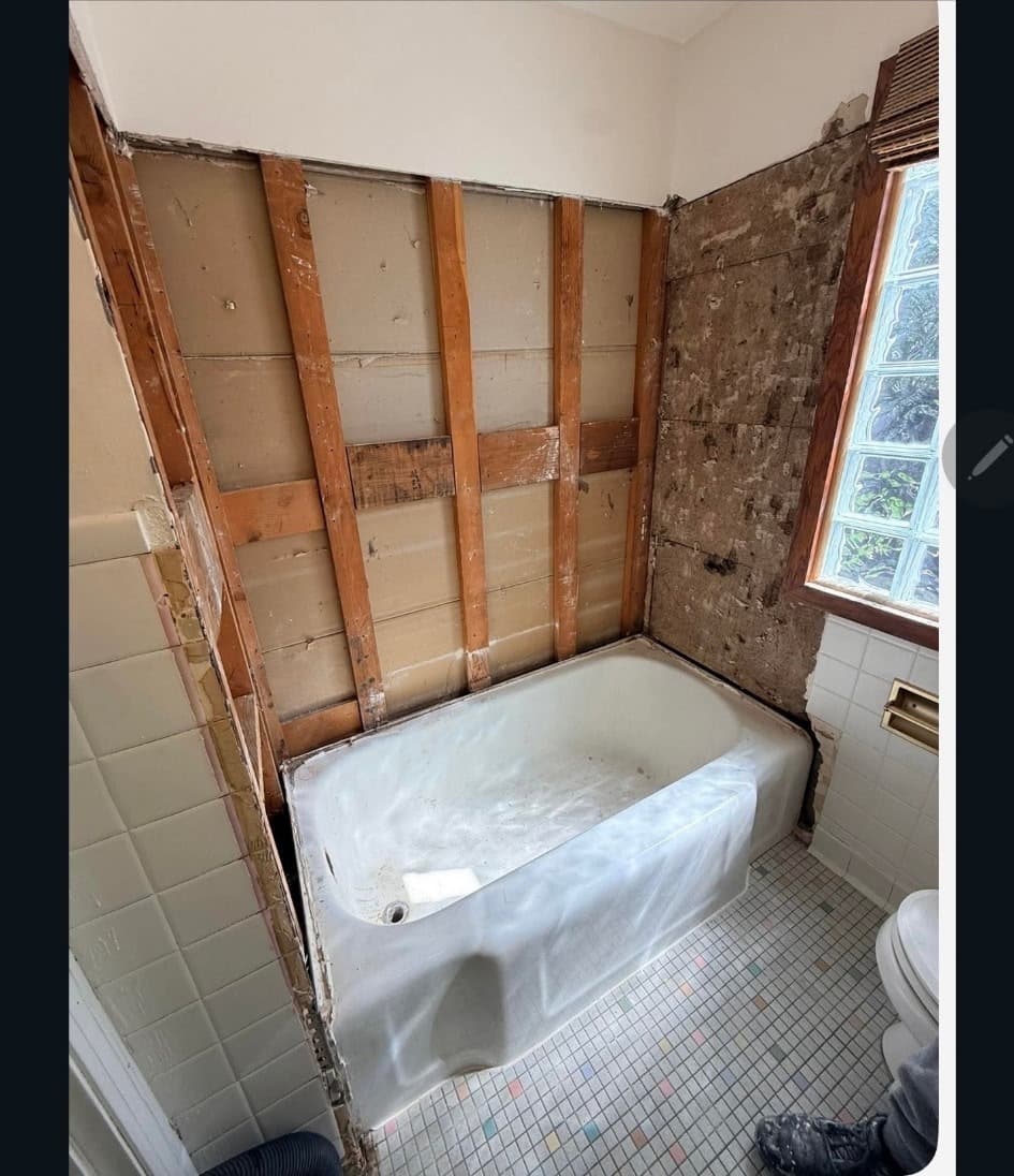 Exposed wall studs behind the tub after tile removal in a Minneapolis bathroom remodel