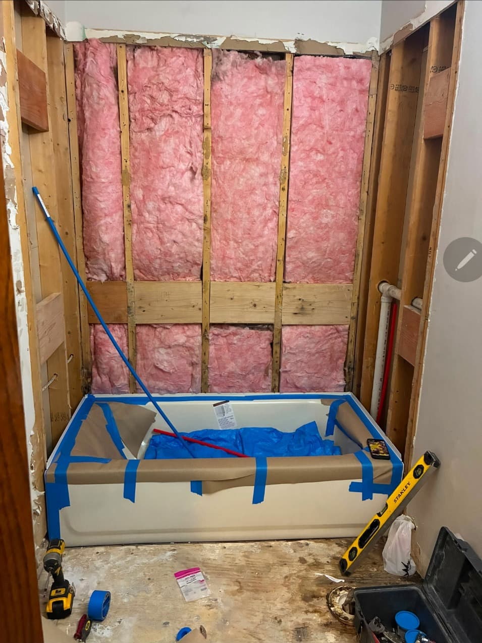 Tub alcove framing and insulation protected with tape and plastic before a new shower surround is installed